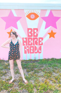 girl in front of be here now wall mural
