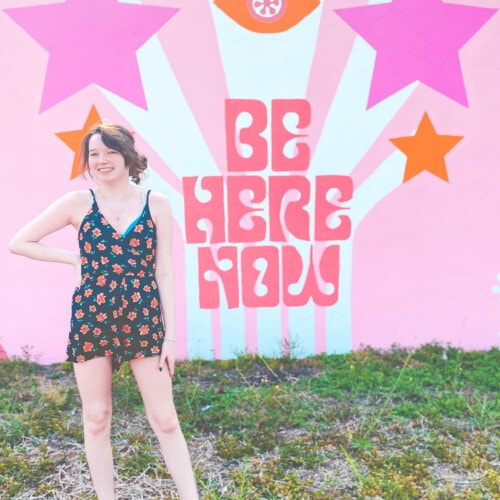 girl in front of be here now wall mural