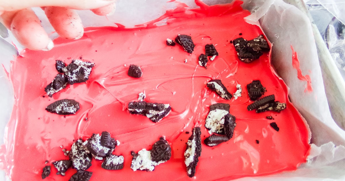 in-process step of adding crushed oreos to the top of chocolate to make mickey bark treat