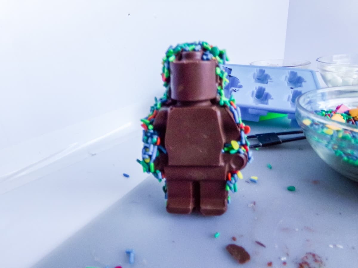 adding sprinkles to the edges of a Lego Man Hot Cocoa Bombs