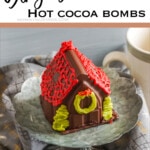 gingerbread house hot chocolate bomb on a cupcake stand with text which reads Gingerbread House Hot Cocoa Bombs