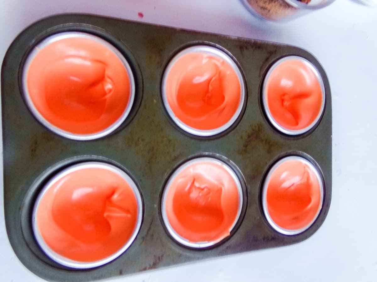 in-process step of filling molds with chocolate to make Orange Slice Candy Hot Cocoa Bombs