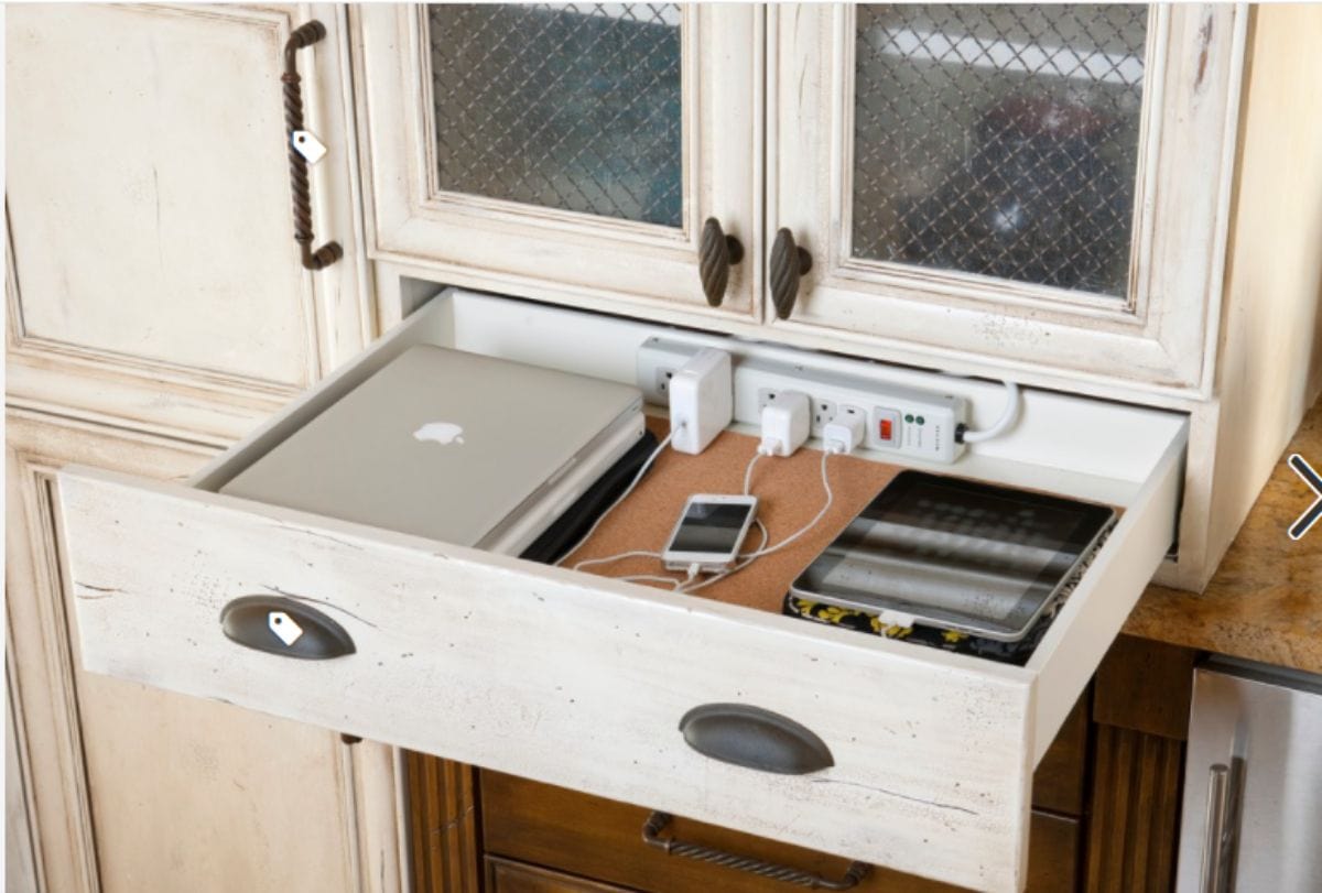 A cream dresser has a drawer open. Inside the drawer is a laptop, phone and ipad. At the back of a drawer is a power bank which the devices are plugged into