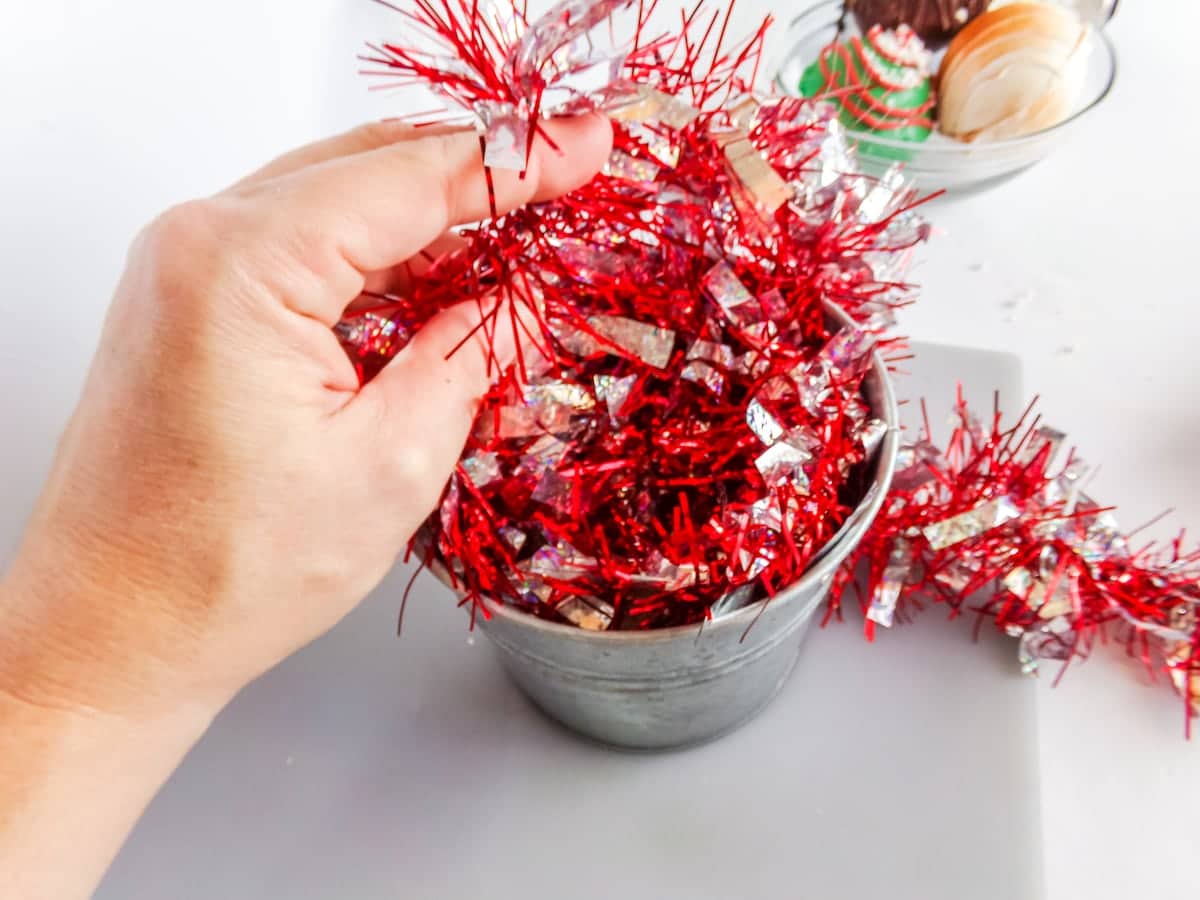 in-process step of adding tinsel into a bucket to make a neighbor gift idea for hot cocoa bombs