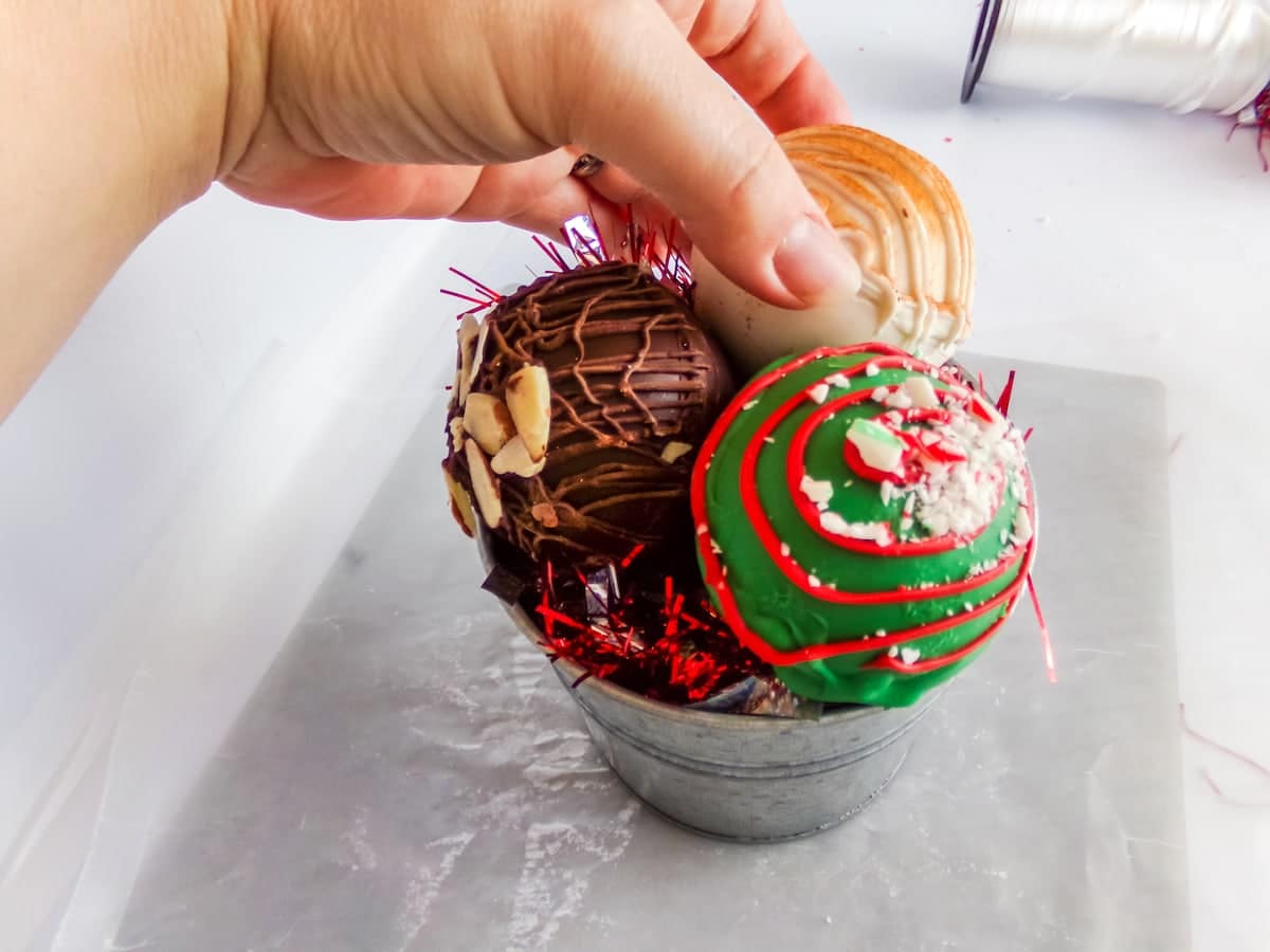adding hot cocoa bombs to a container to make a dollar tree hot cocoa bomb neighbor gift