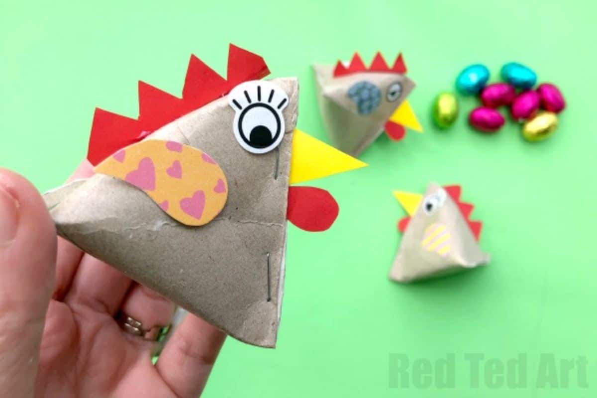 a hand holds a pyramid of paper decorated to look like a chicken, with 3 more in the background