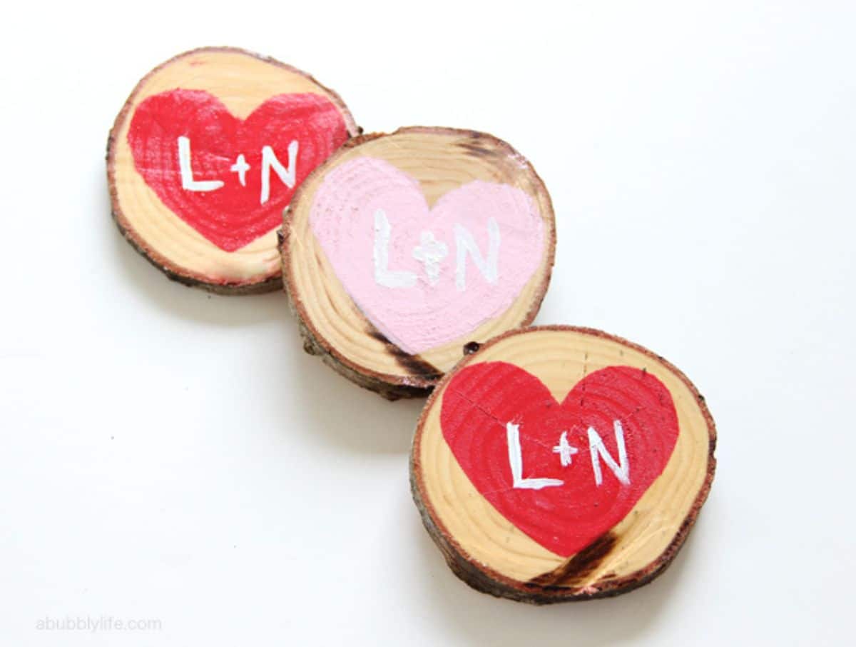 On a white background, 3 wood slices are decorated with red and pink hearts. Inside the hearts are the letters "L + N"