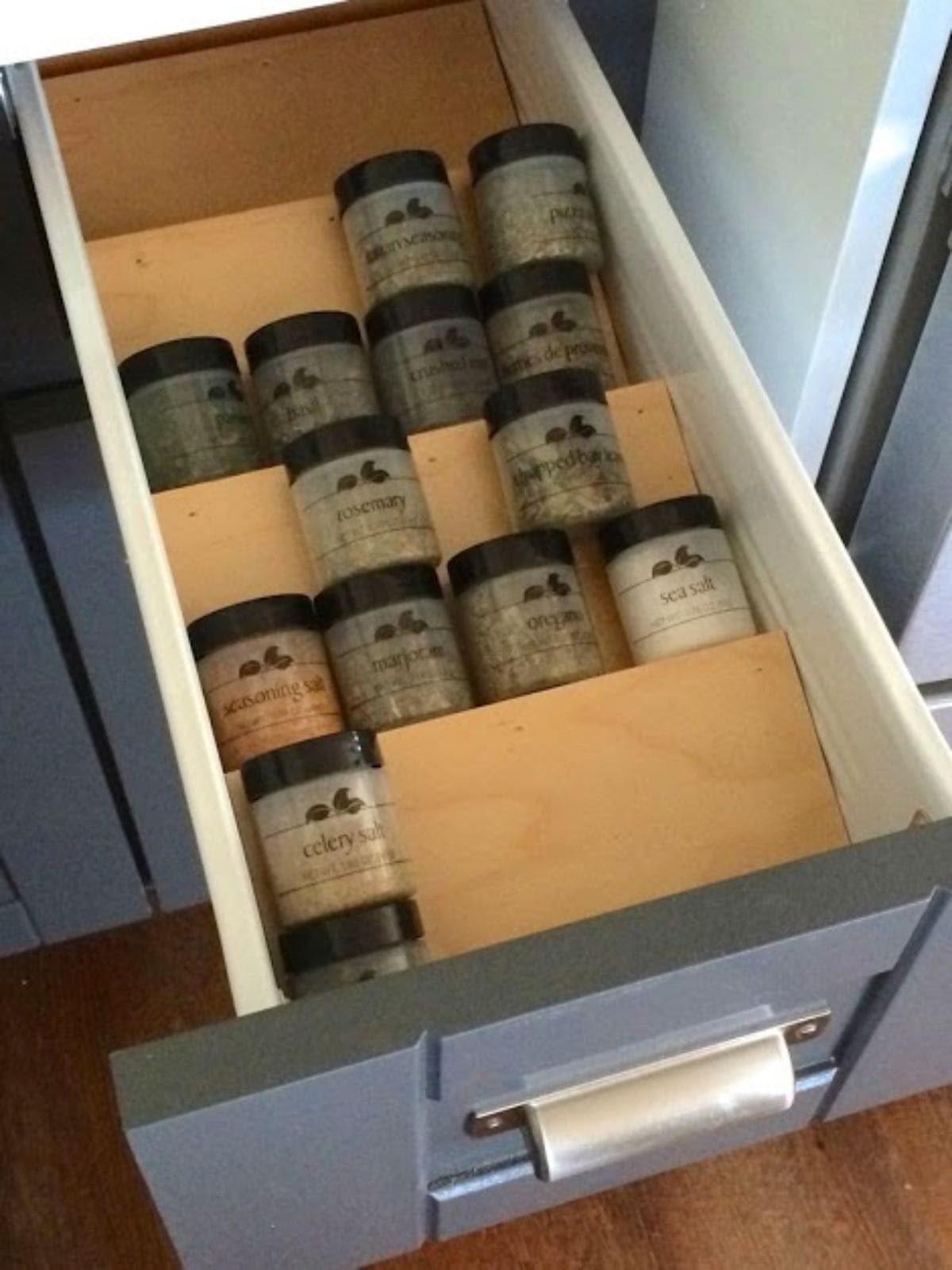 Inside a kitchen drawer are some slanted pieces of wood. On each shelf are small galss spice pots 