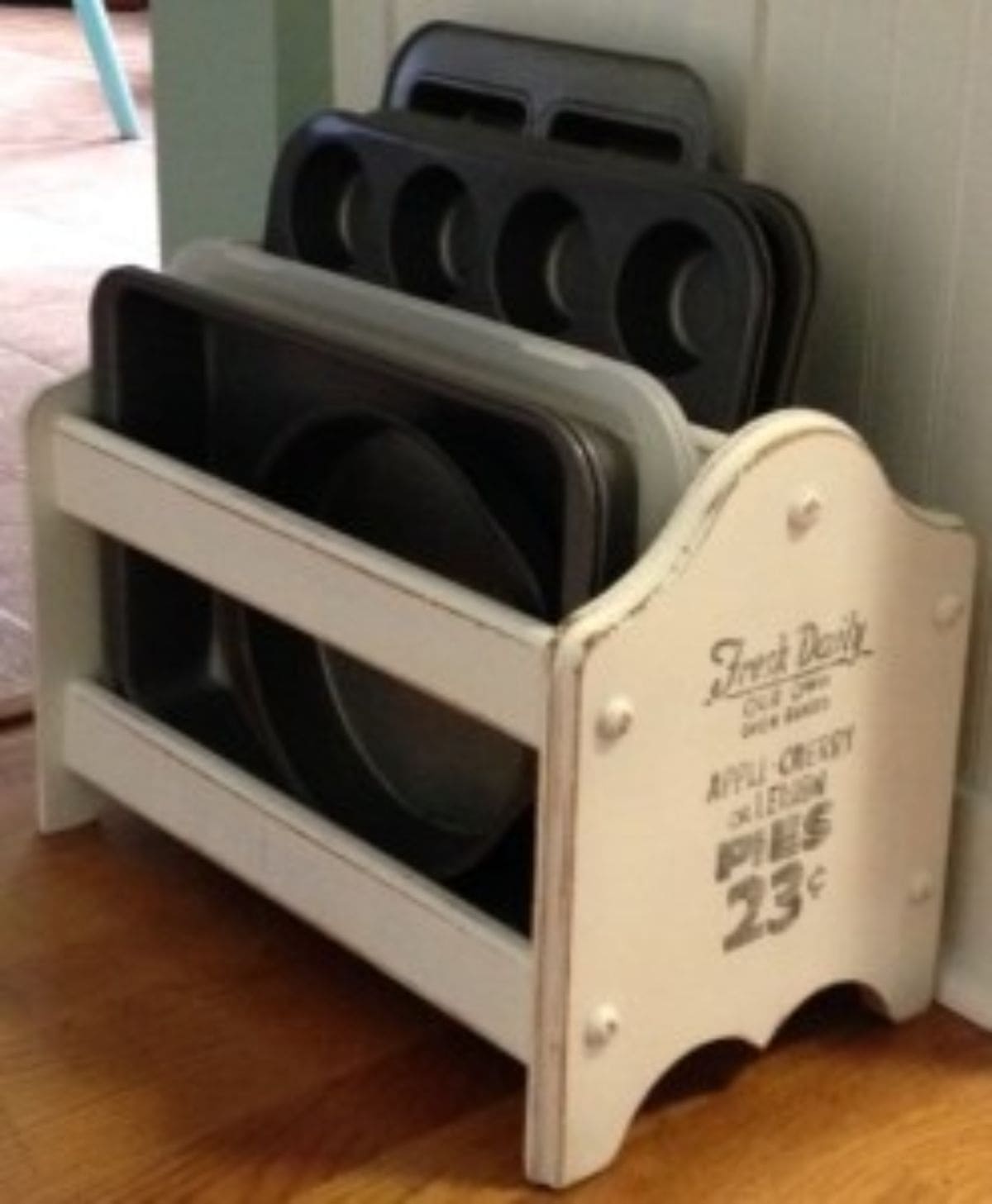 A cream shabby chic magazine rack has been repurposed to hold muffin trays and baking trays