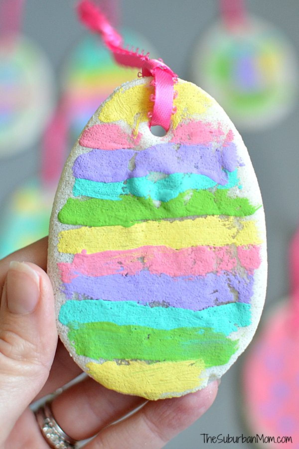 a hand holds up a striped egg made of salt dough with a ribbon attached to the top