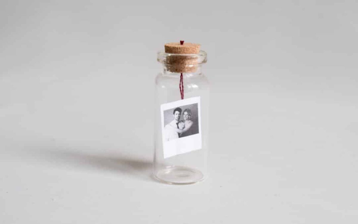 A glass bottle with a cork stopper sits on a surface. Inside is a black and white photograph suspended from the stopper