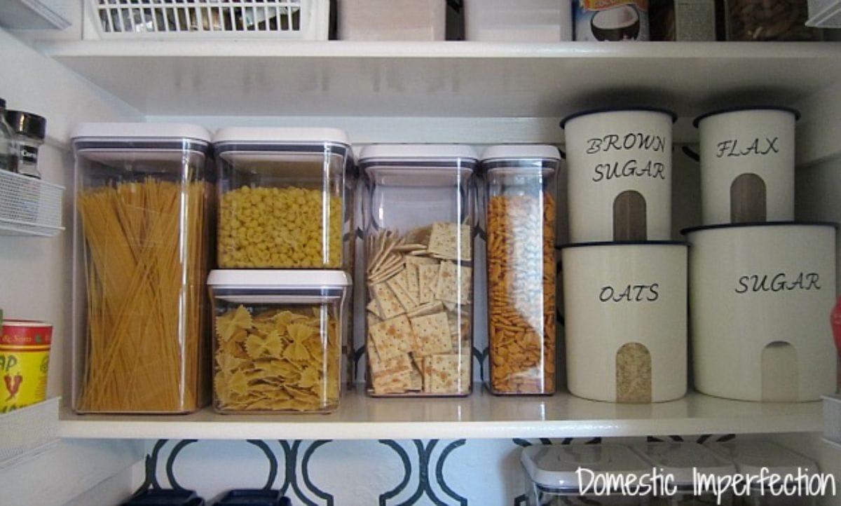 The inside of a pantry showing glass square containers with white lids, containing dry goods.