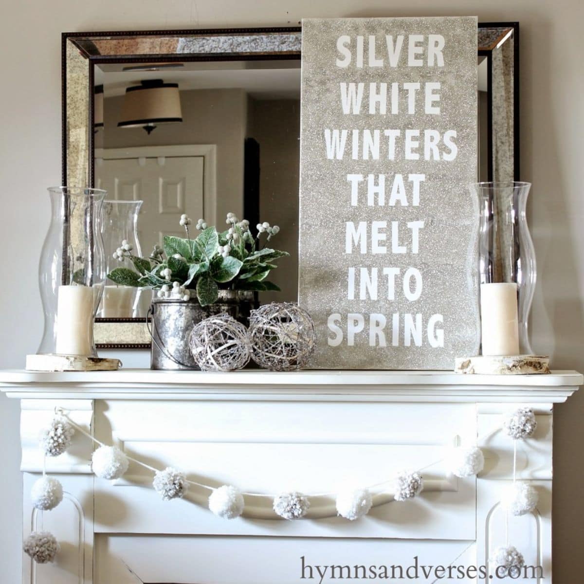 On a white mantelpiece in front of a mirror is a sign with white letters that reads "Silver white winters that melt into spring"