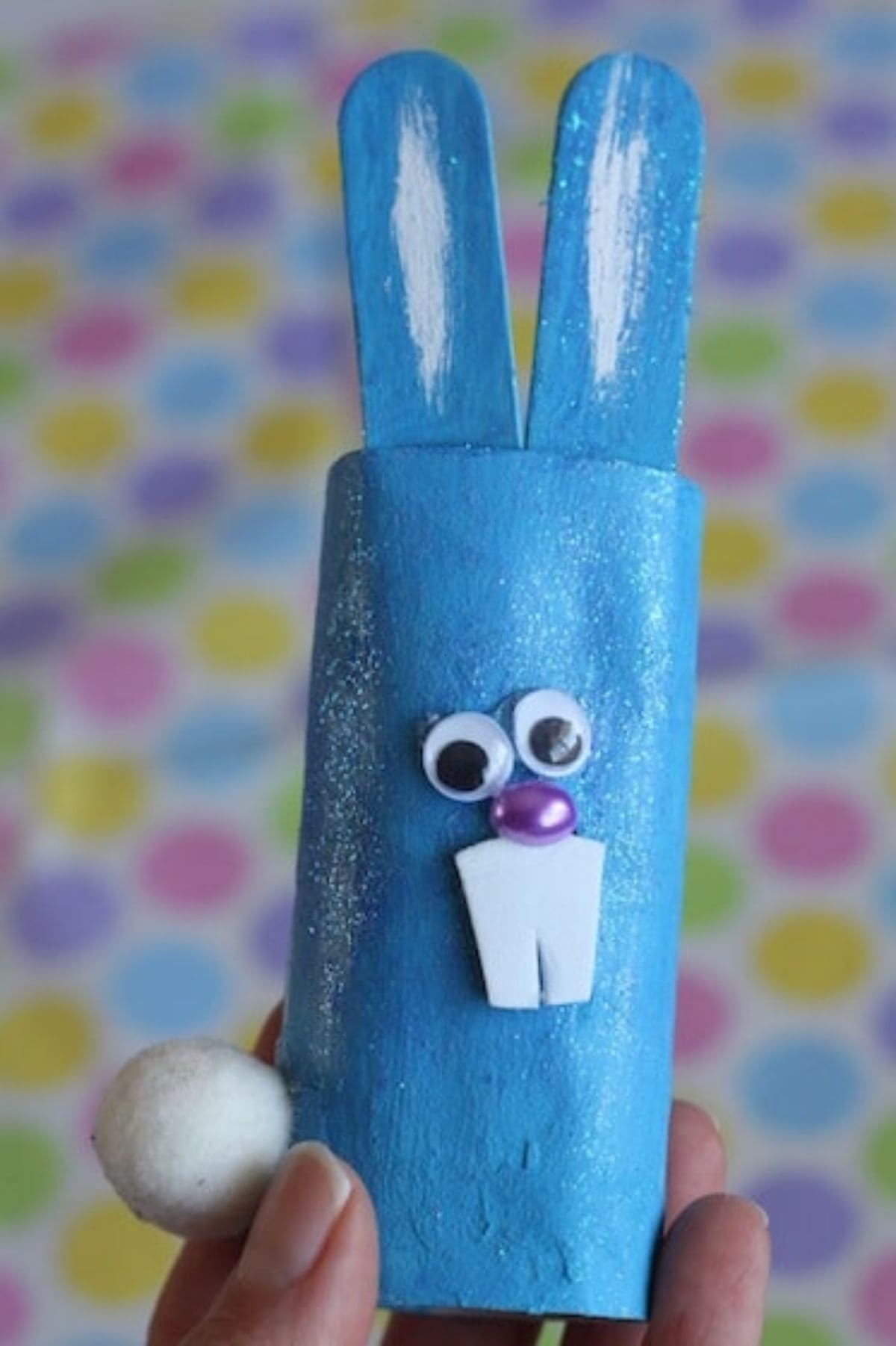 a hand holds a toilet roll painted blue and decorated to look like a rabbit