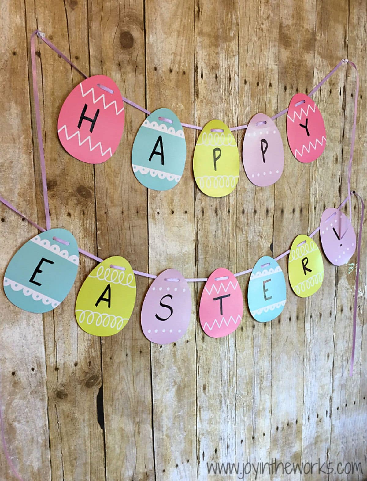 a garland of striped eggs spelling out Happy Easter hang on strings against a wooden backdrop