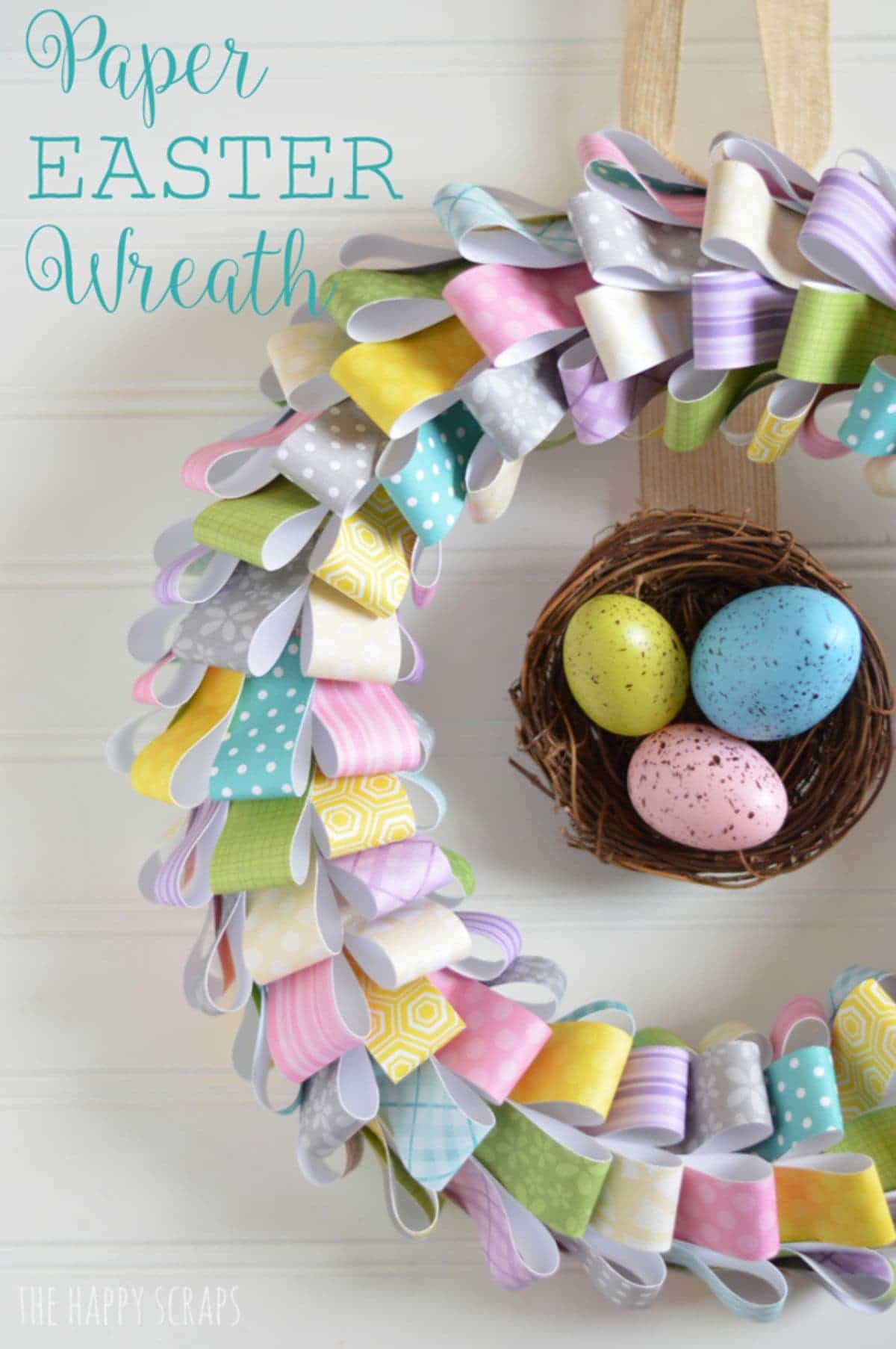 on a white background a wreath made of folded colored paper surrounds a twig basket with chocolate eggs inside