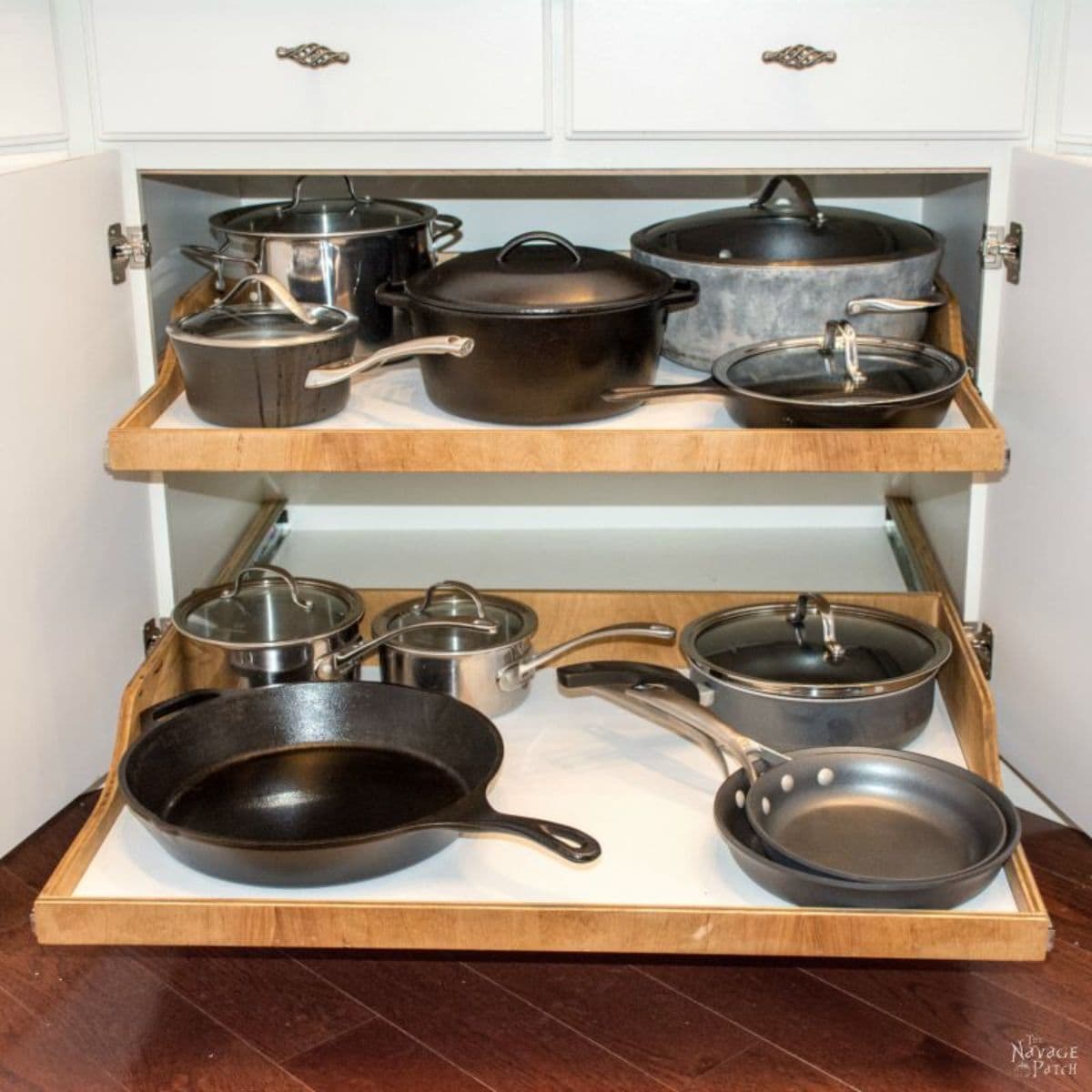 The inside of a kitchen cabinet is shown with 2 sliding shelves slightly oulled out. Each shelf holds pots and pans