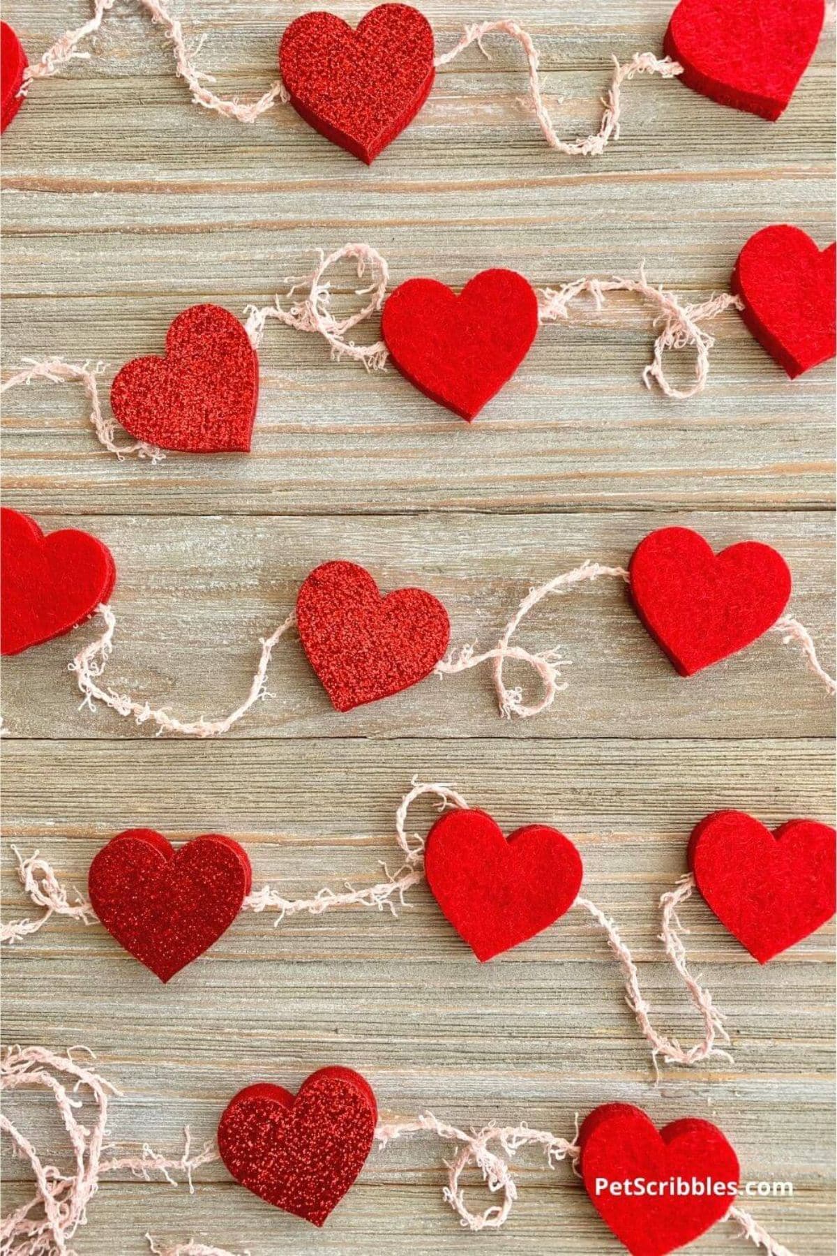 On a wooden background are 3 strongs of red felt hearts