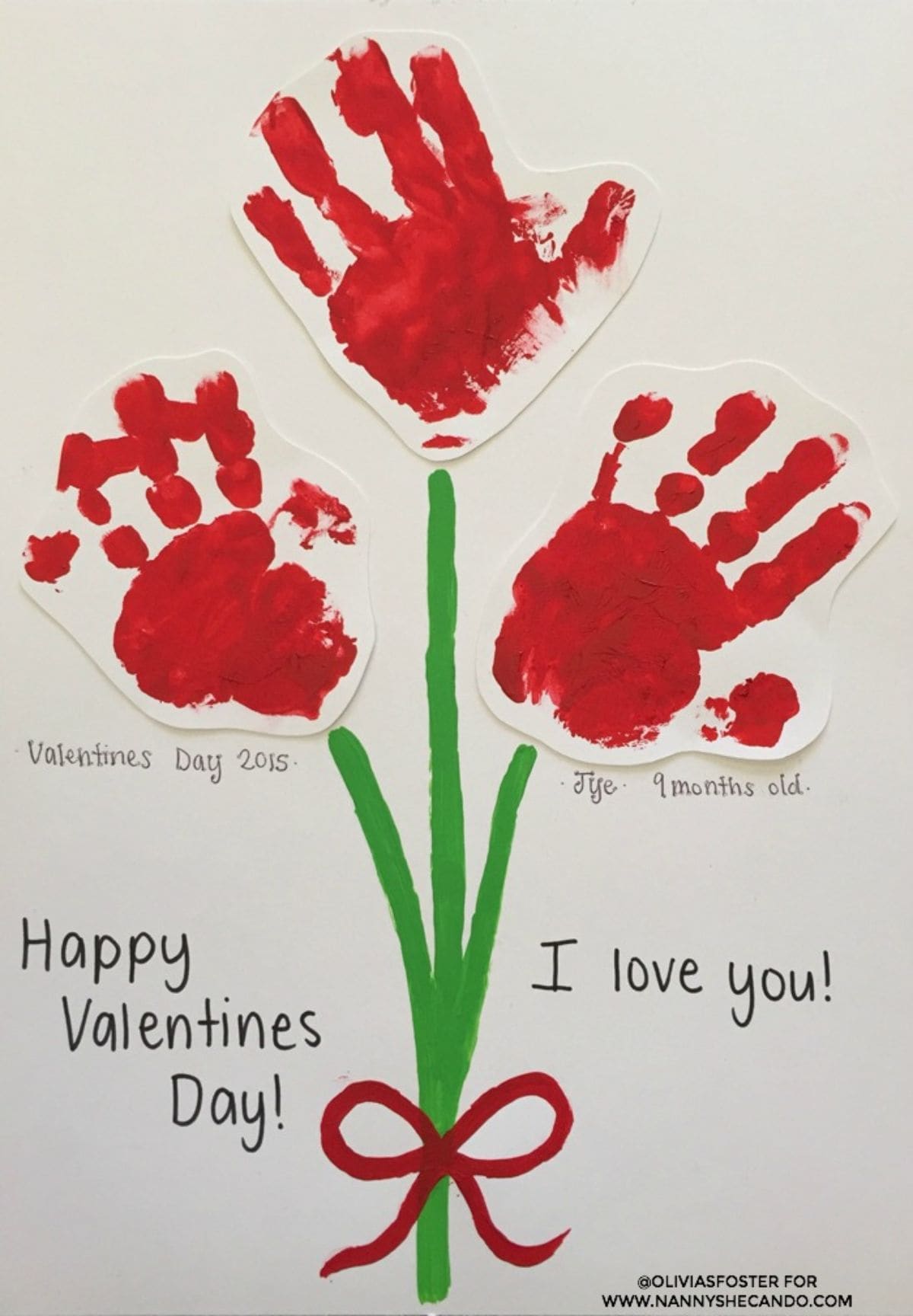 A child's drawing of a bunch of flowers made up of green painted stems with a red painted bow, and 3 red handprints as flowers. The text reads "Happy Valentine's Day! I love you". Under the left hadn print is "Valentines Dat 2015" under the right hand print is "Tye. 9 months old"