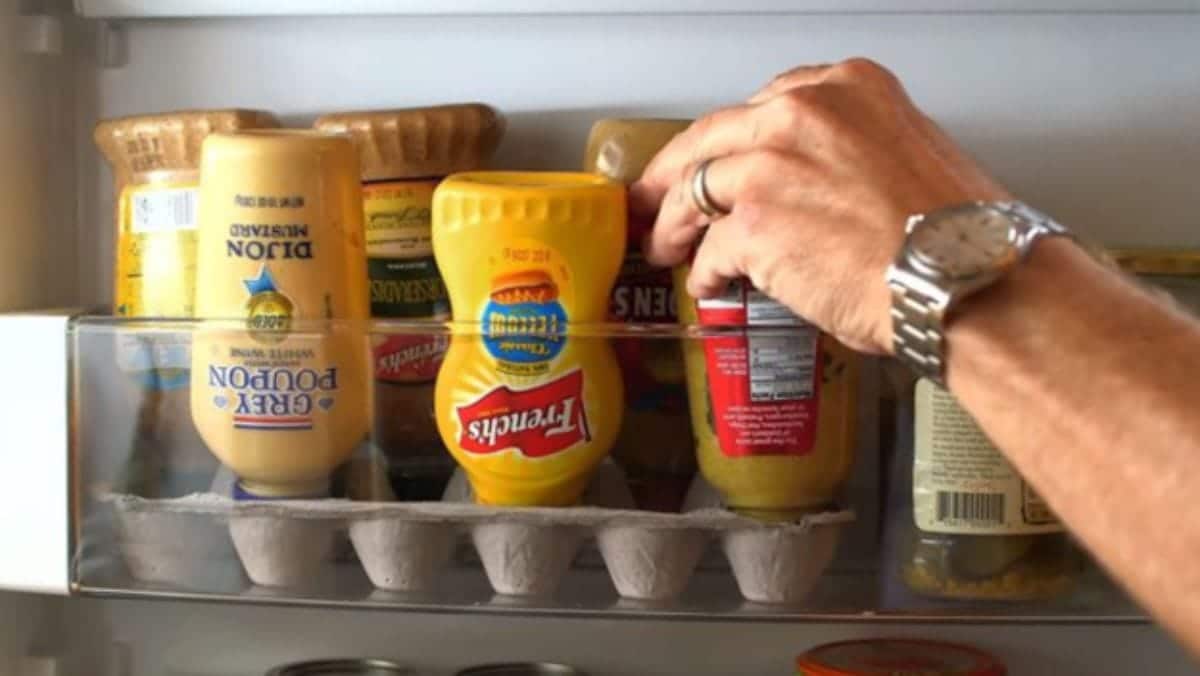 Inside a fridge shelf is the bottom half of an egg box. Upiside down in the egg box are different condiments