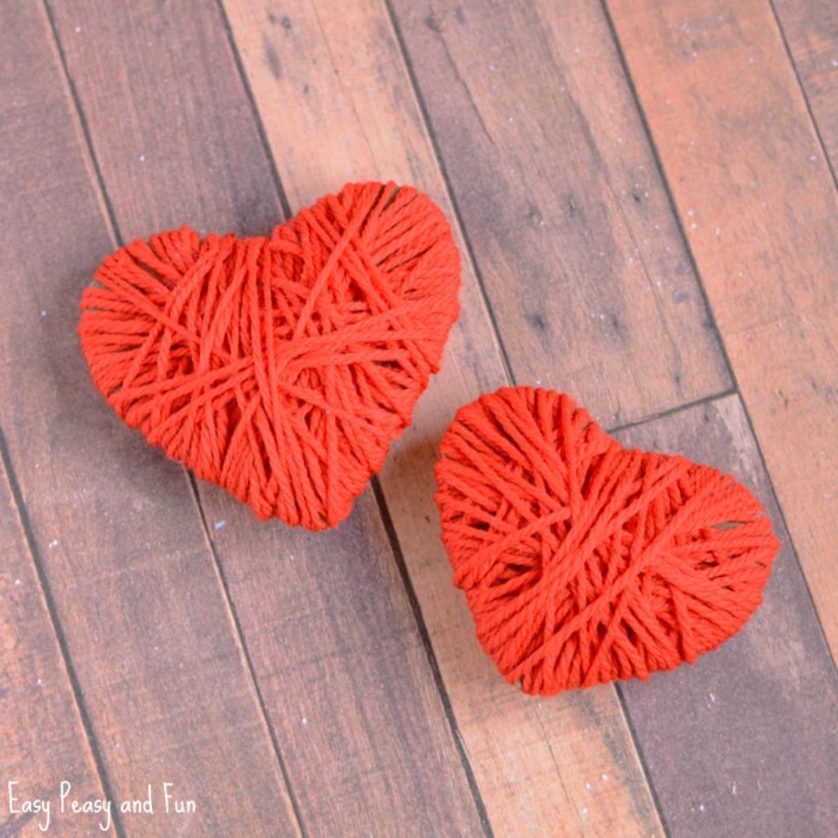 2 red yarn hearts sit on a wooden table