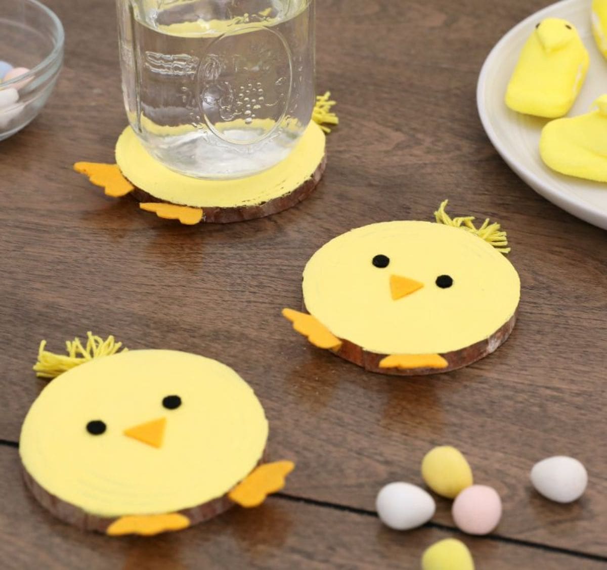 on a wooden table, 3 wooden coasters have been painted to look like yellow chicks. One of them has a mason jar sitting on it