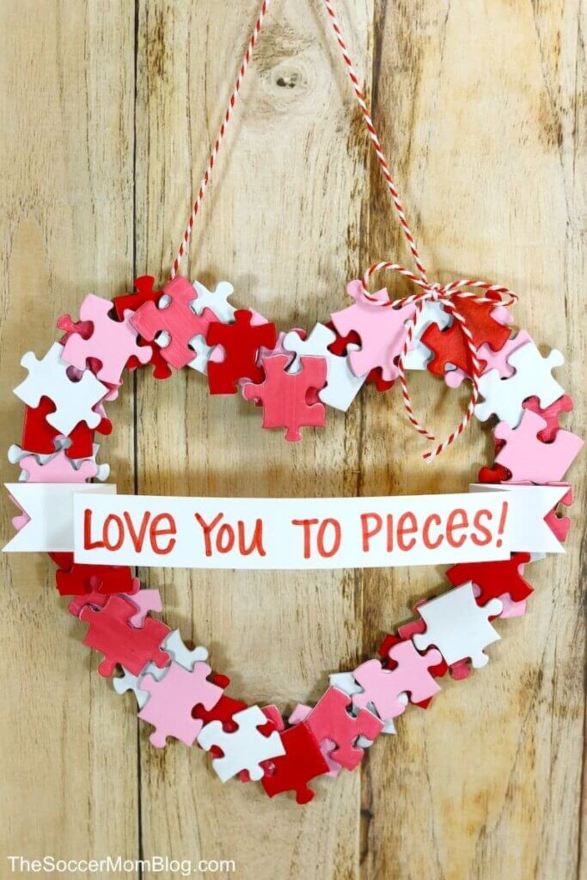 On a wooden background is a heart shape made of red, pink and white puzzle pieces. Across the middle is a scroll shap in white with the red text "Love you to pieces"