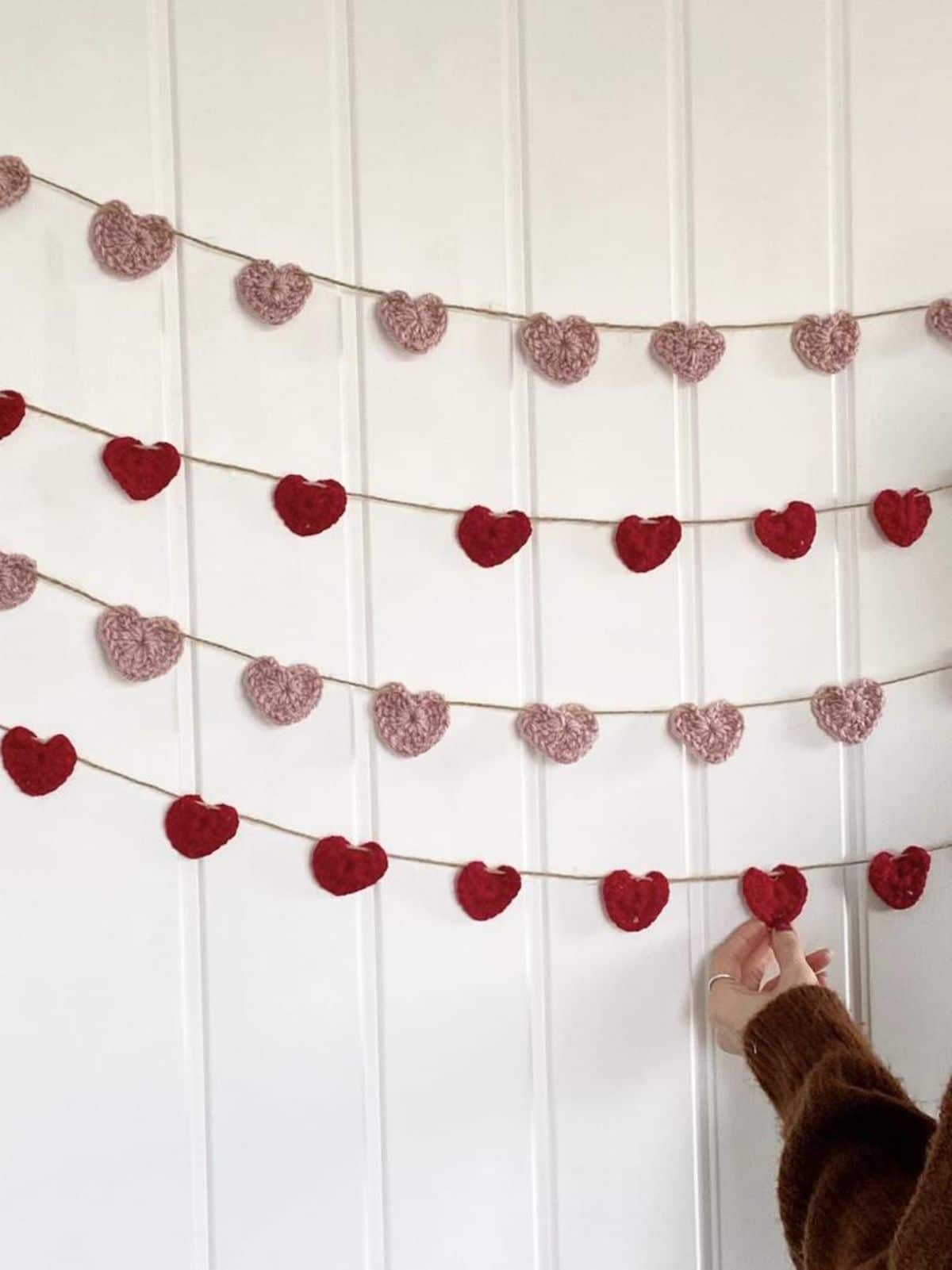 ON a white batten wall are 2 strings of red hearts and 2 strings of pink hearts