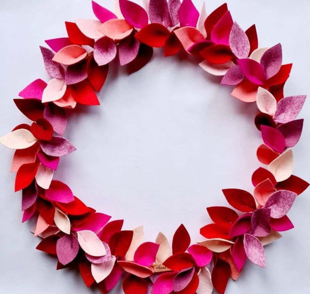 On a white background is a circular wreath made of red, pink and dark pink felt leaves