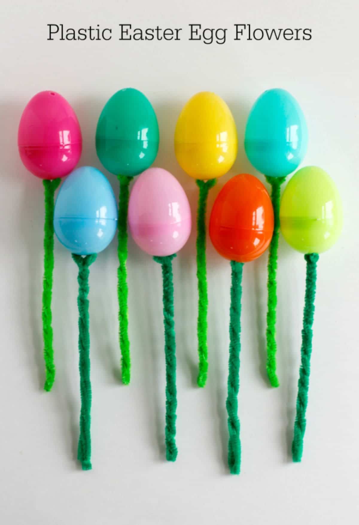 8 colored plastic eggs have been stuck on top of 8 green pipe cleaners on a white background