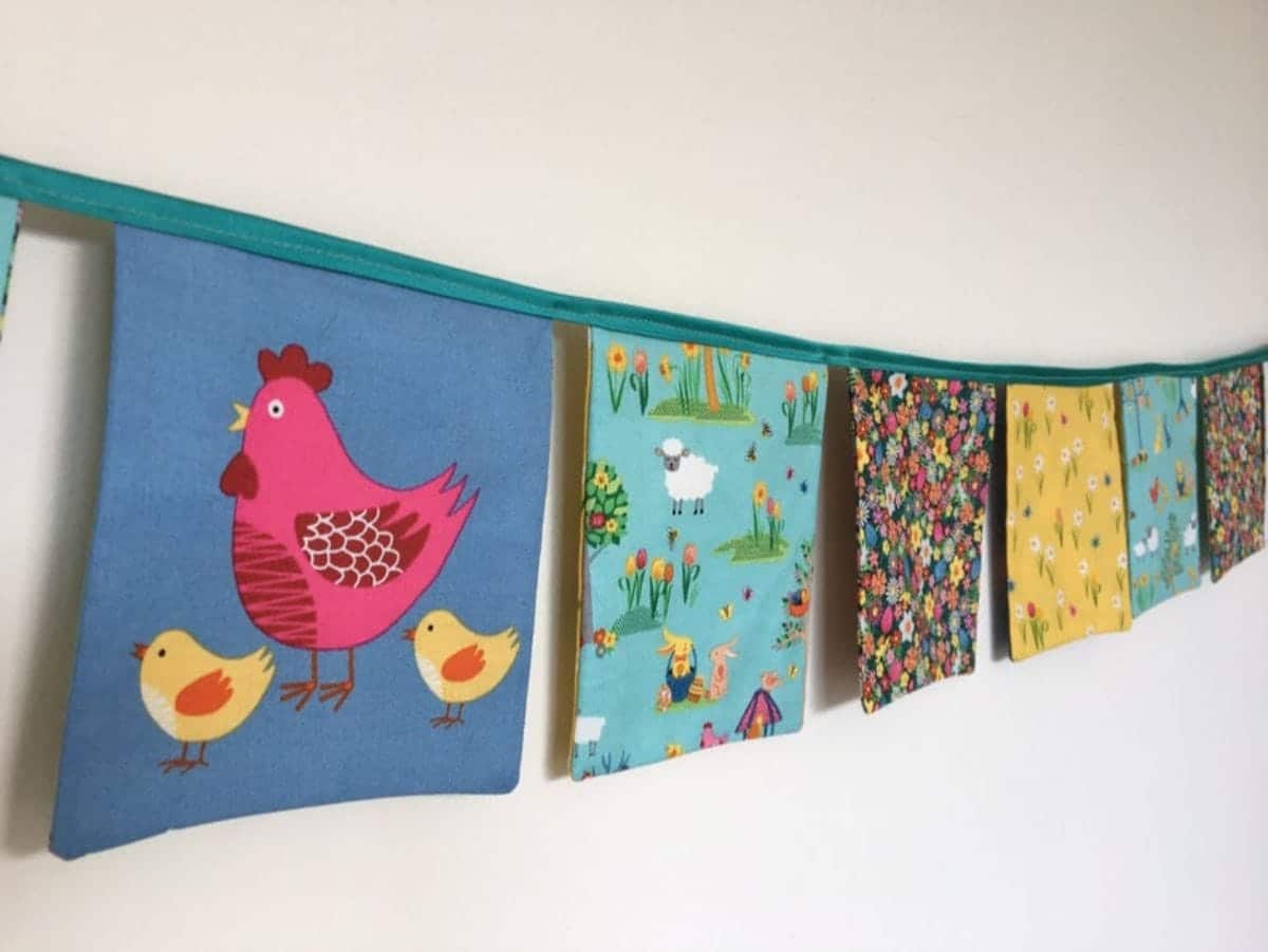 a garland of fabric squares hangs on a wall. One has a red chicken on it, others have different colored flower fabrics.