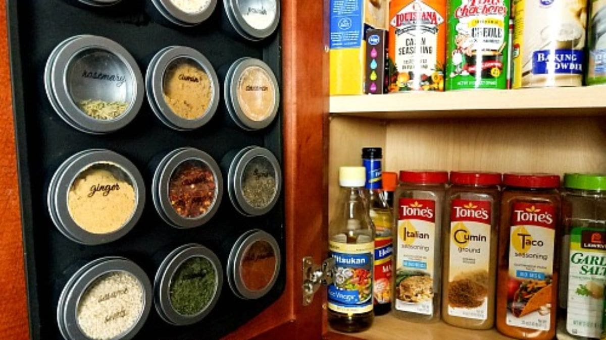 an open cupbaord, with packets and bottles on the shelves on the right hand side of the picture. The door has been painted in black paint and circular metal spice jars are stuck to it with magnets