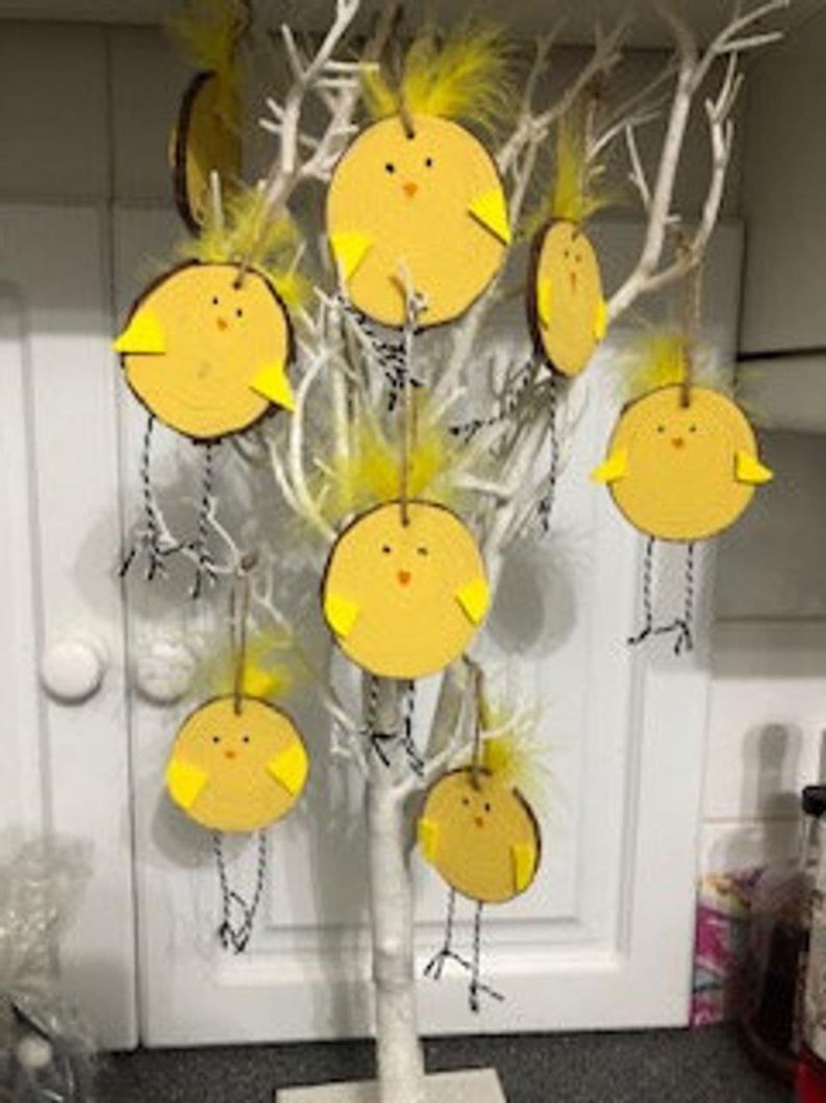 Hanging from an easter tree are 8 wooden slices decorated in yellow to look like chicks