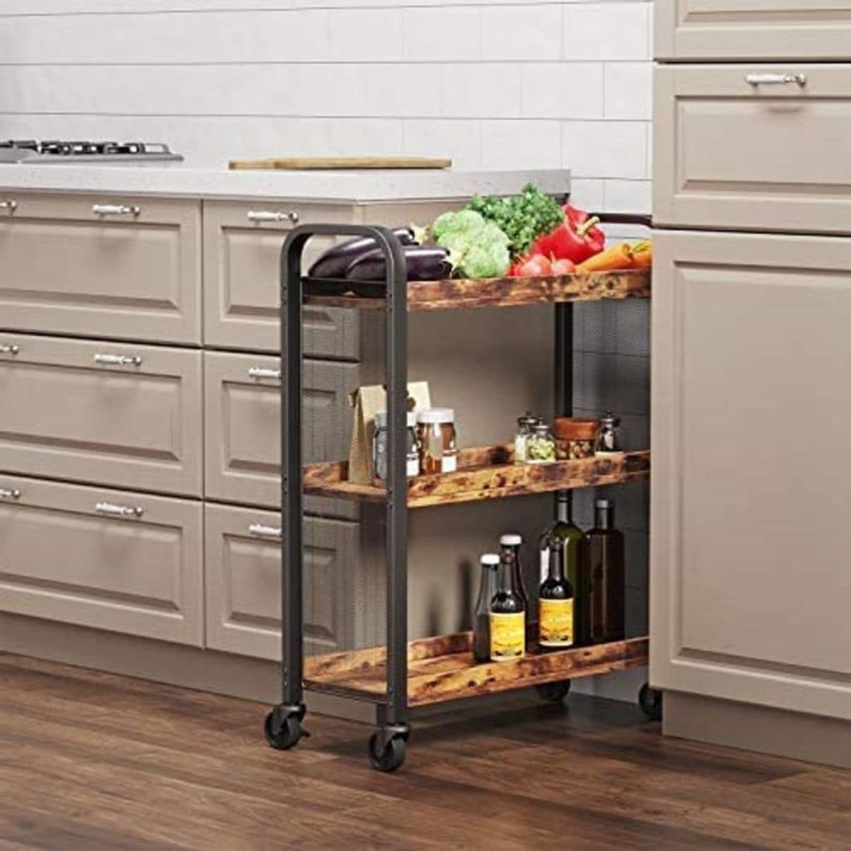 in front of a cream kitchen is a wheeled trolley with 3 tiers made of sarker metal and wooden shelves. Vegetables, condments and bottles sit on the shelves.