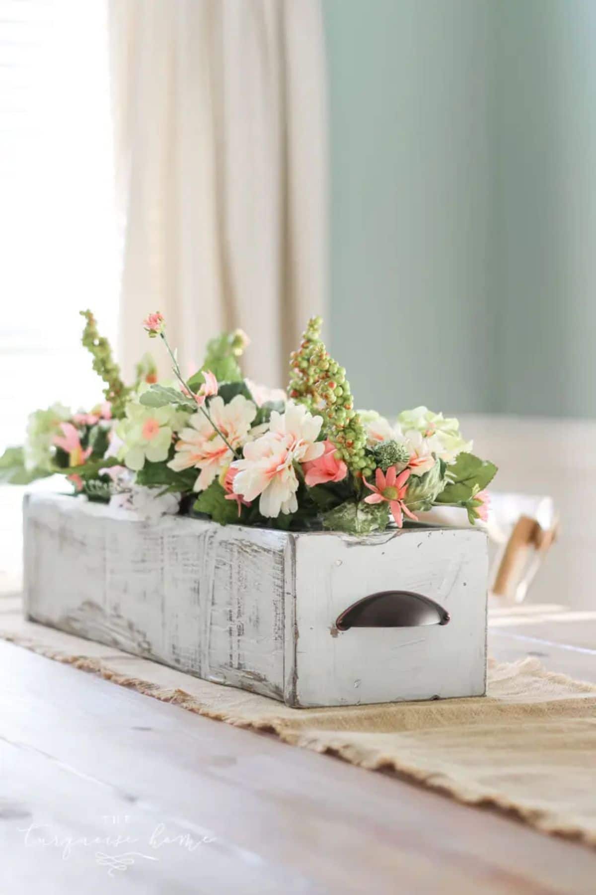 on a wooden table, sitting on top of a table runner is a shabby chic painted crate filled with pin kand white flowers