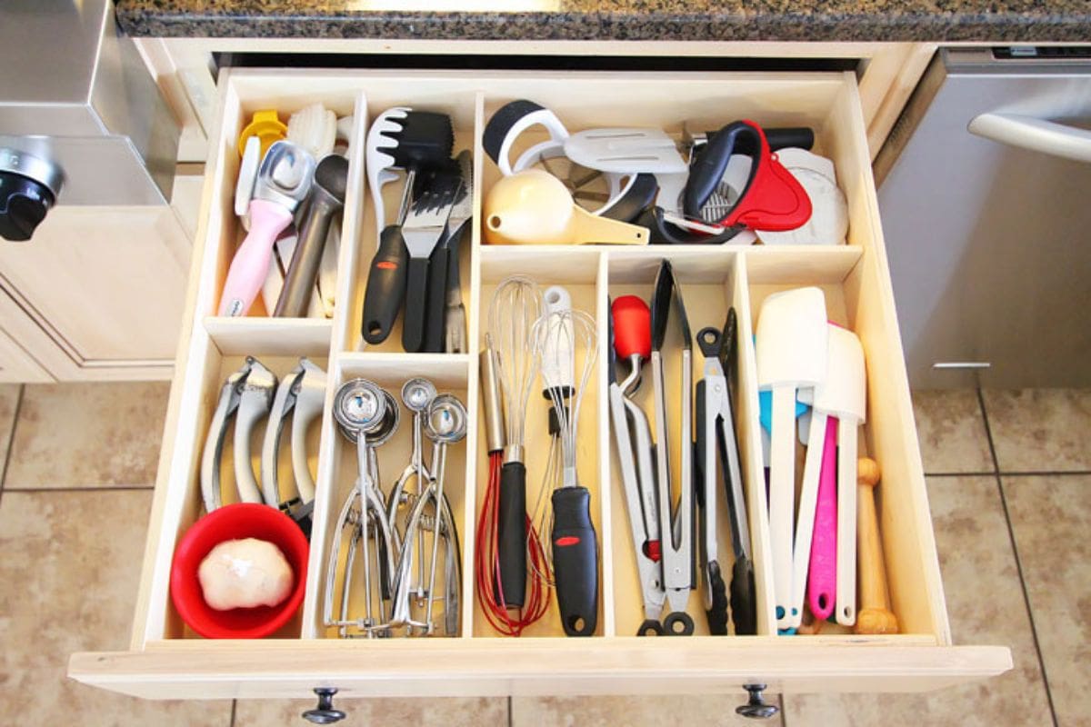 The inside of a kitchen drawer has been divided into sections with wood. Kitchen utensils sit in each section