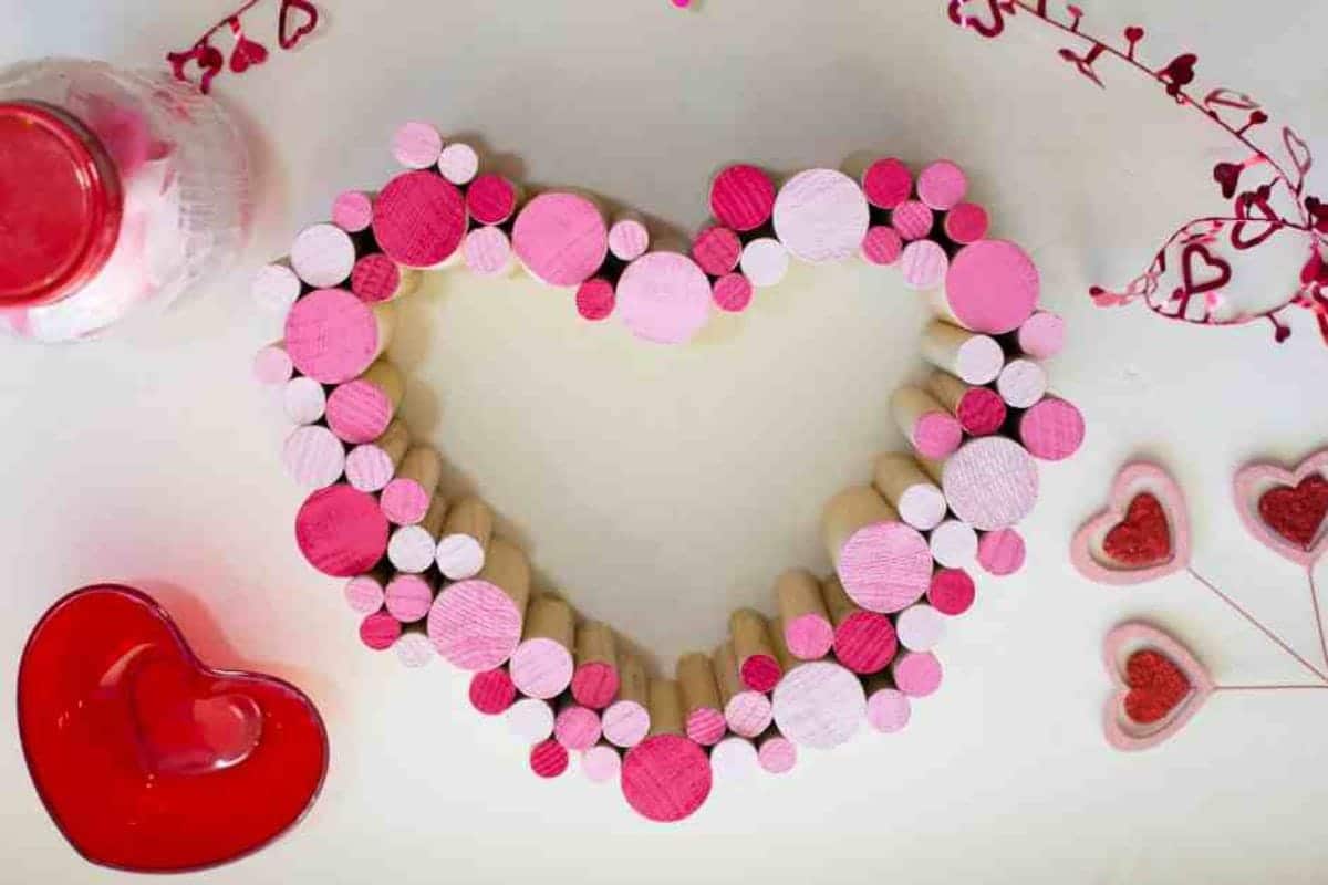 On a white background, a heart shape has been made out of dowel sections of different widths in differetn shades of pink.