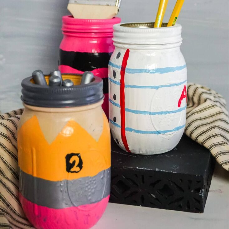 pencil paper and crayon painted jars on a table