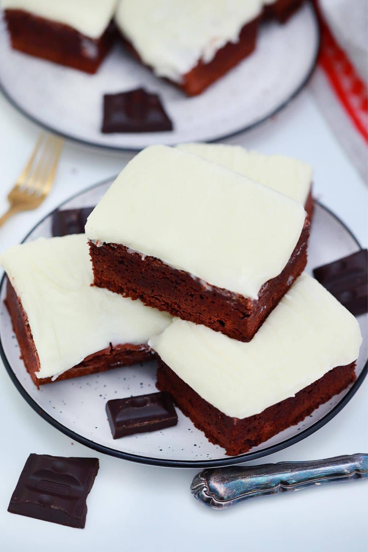 three iced brownies stacked on a white plate
