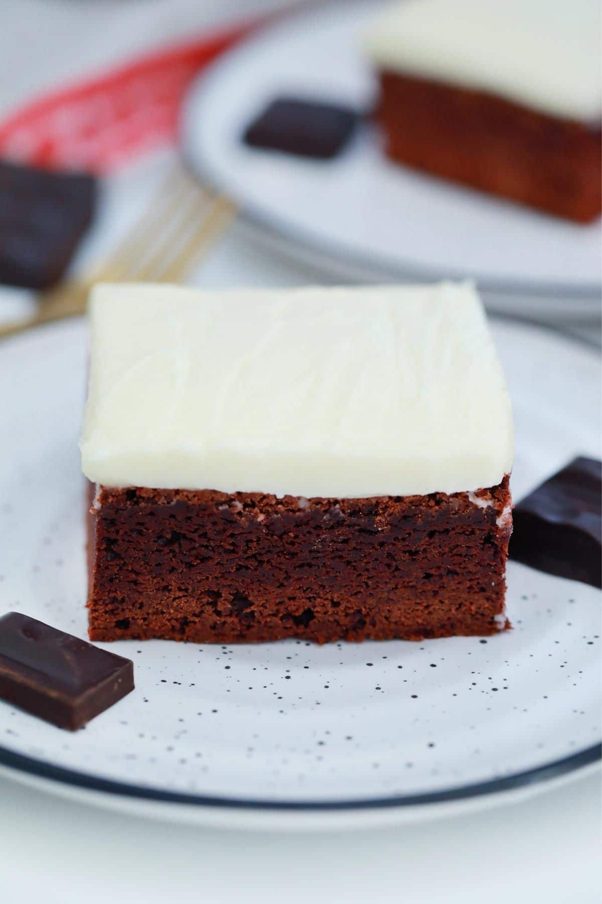 single slice of red velvet brownie with icing on white saucer