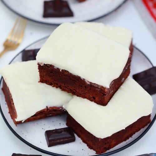 three iced brownies stacked on a white plate